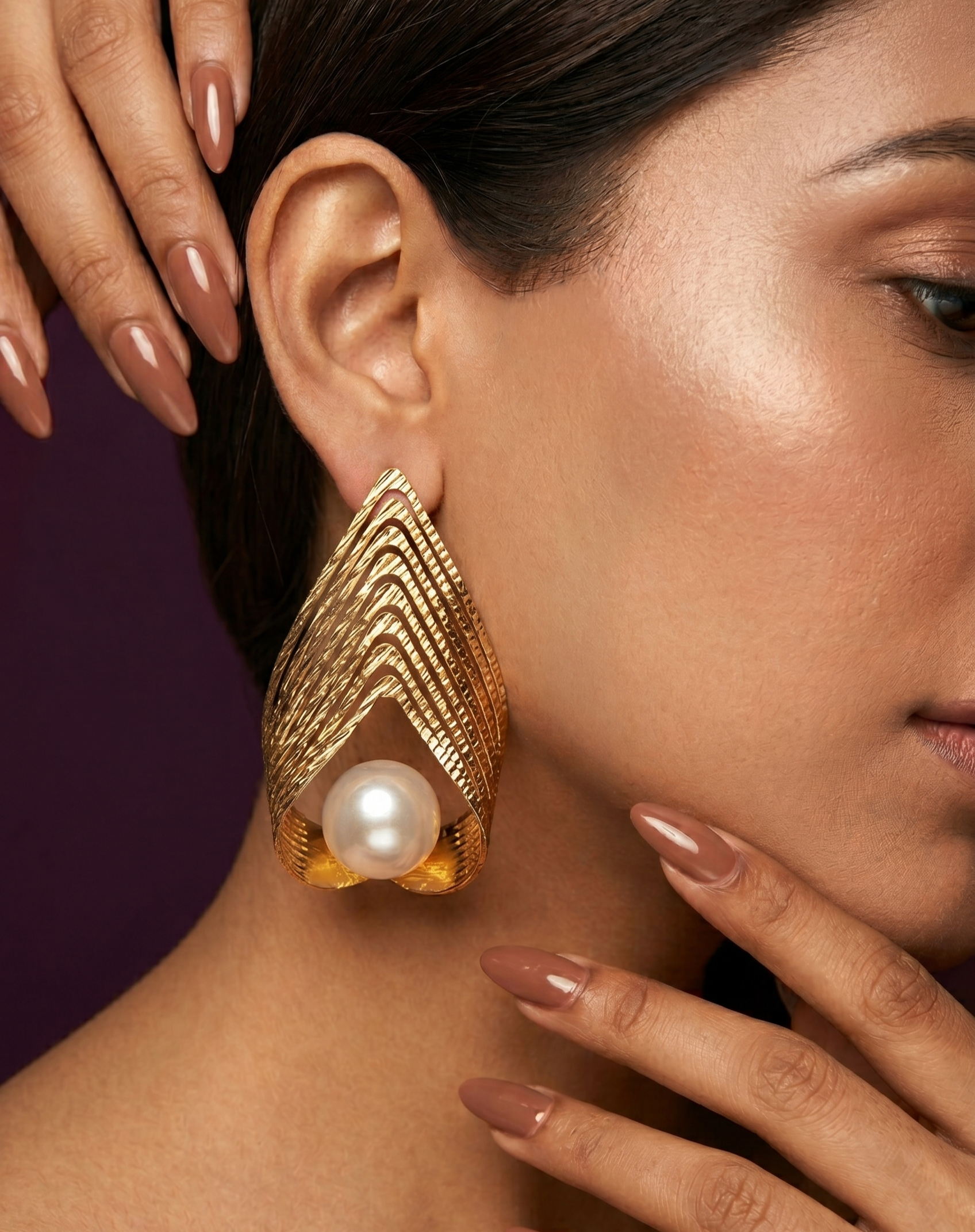 Gold earrings with a pearl worn by a woman against a dark background