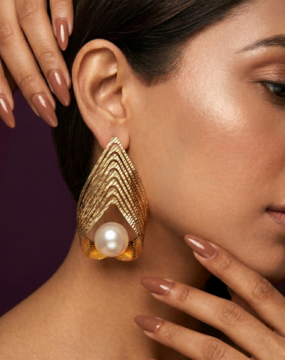 Gold earrings with a pearl worn by a woman against a dark background