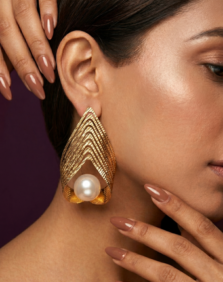 Gold earrings with a pearl worn by a woman against a dark background