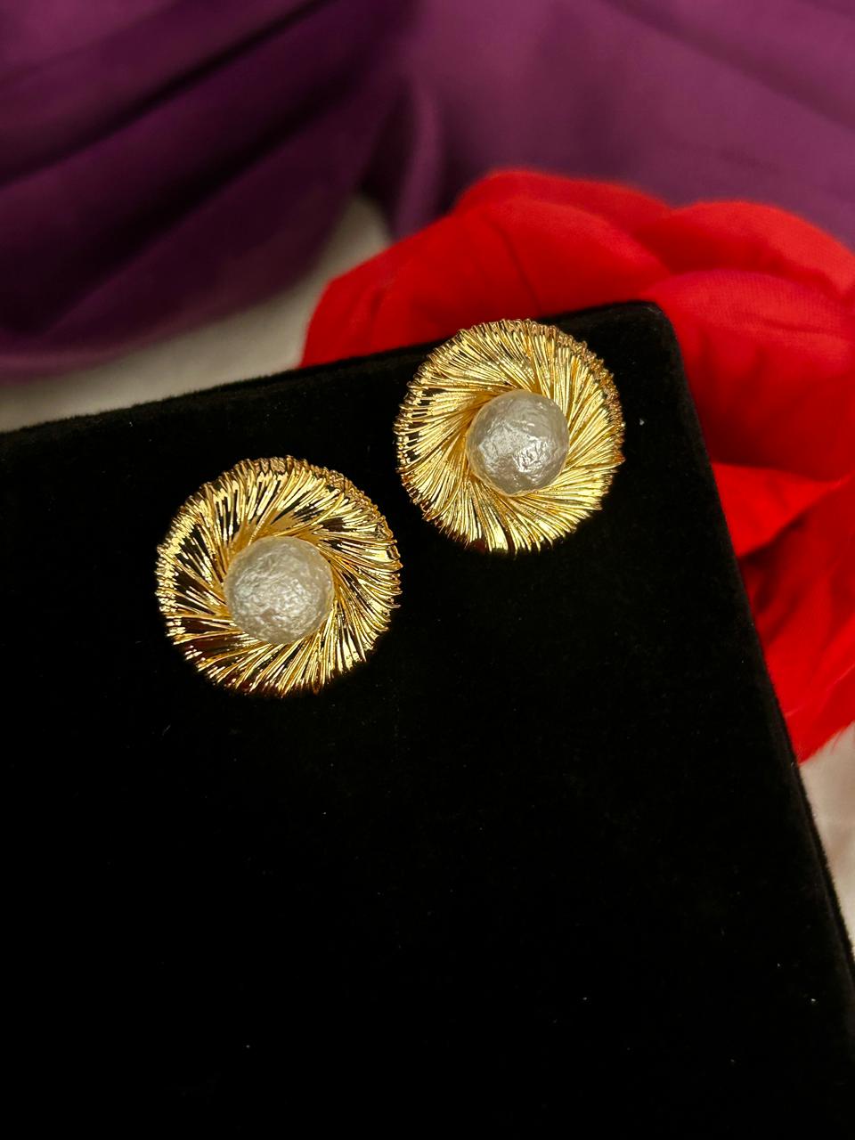 Gold earrings with a textured design on a black stand with a red fabric background