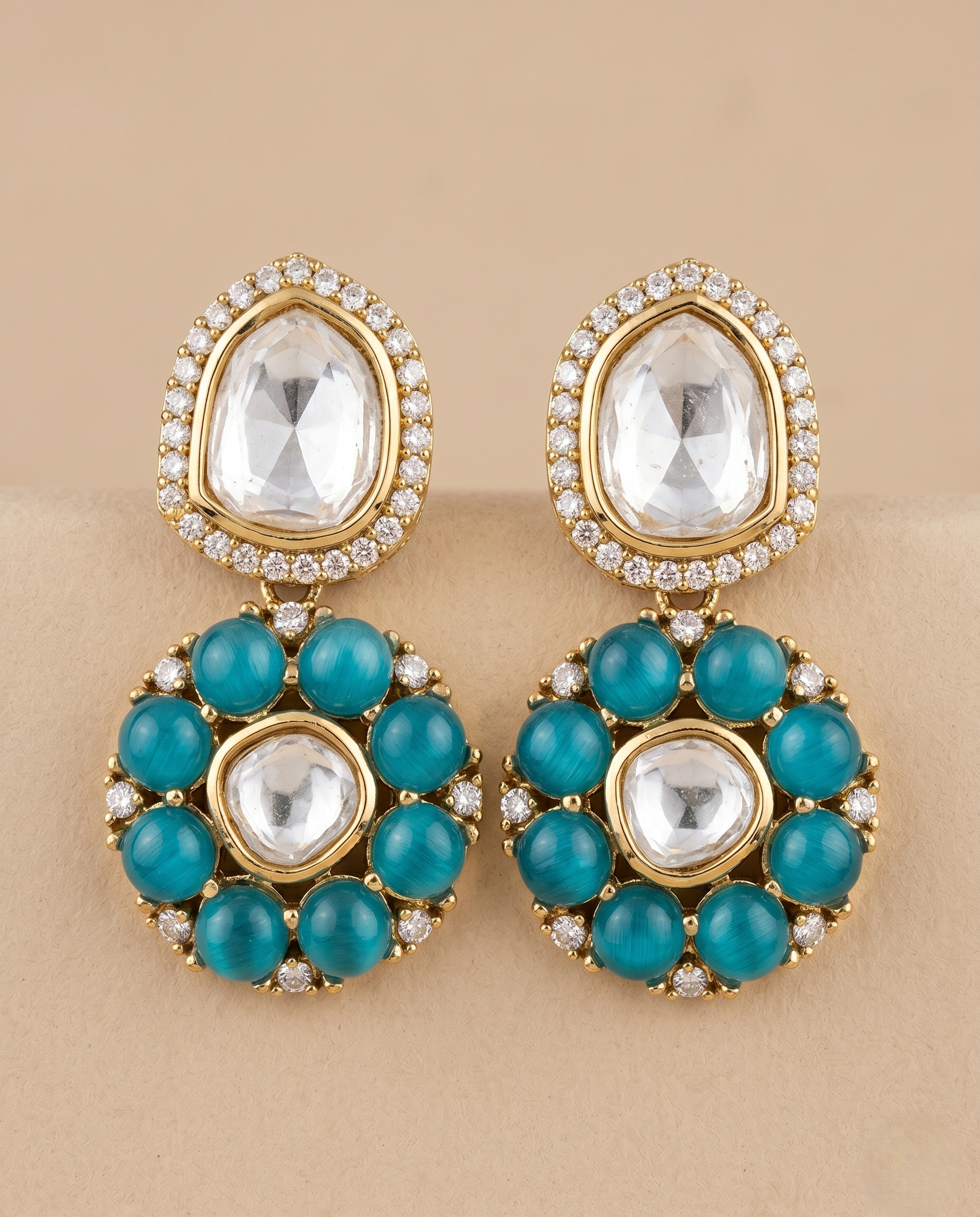 Gold earrings with clear and  blue gemstones on a beige background