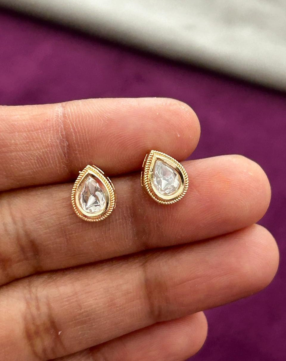 Gold earrings with clear gemstones held between fingers against a purple background