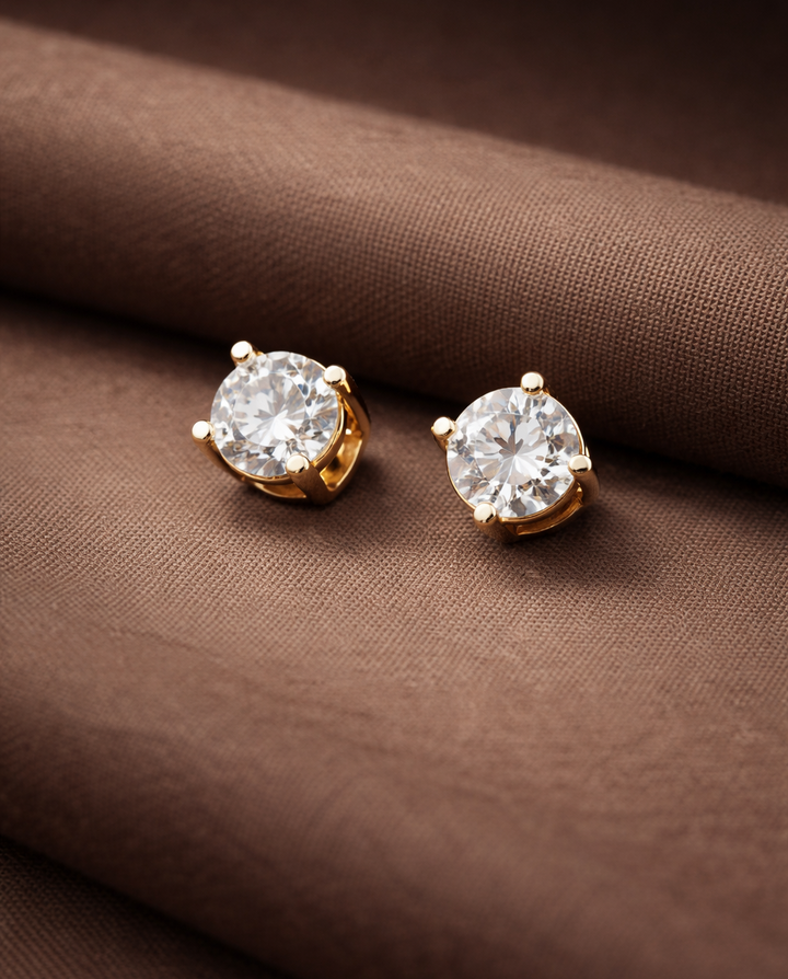 Gold earrings with clear gemstones on a brown fabric background