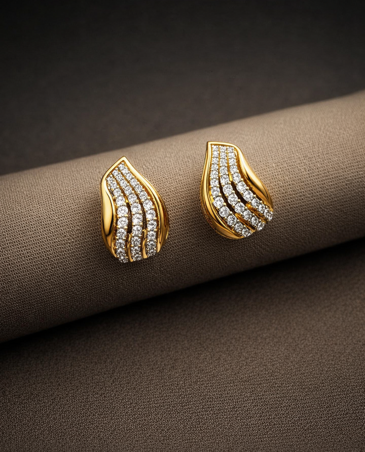 Gold earrings with diamond accents on a brown fabric background