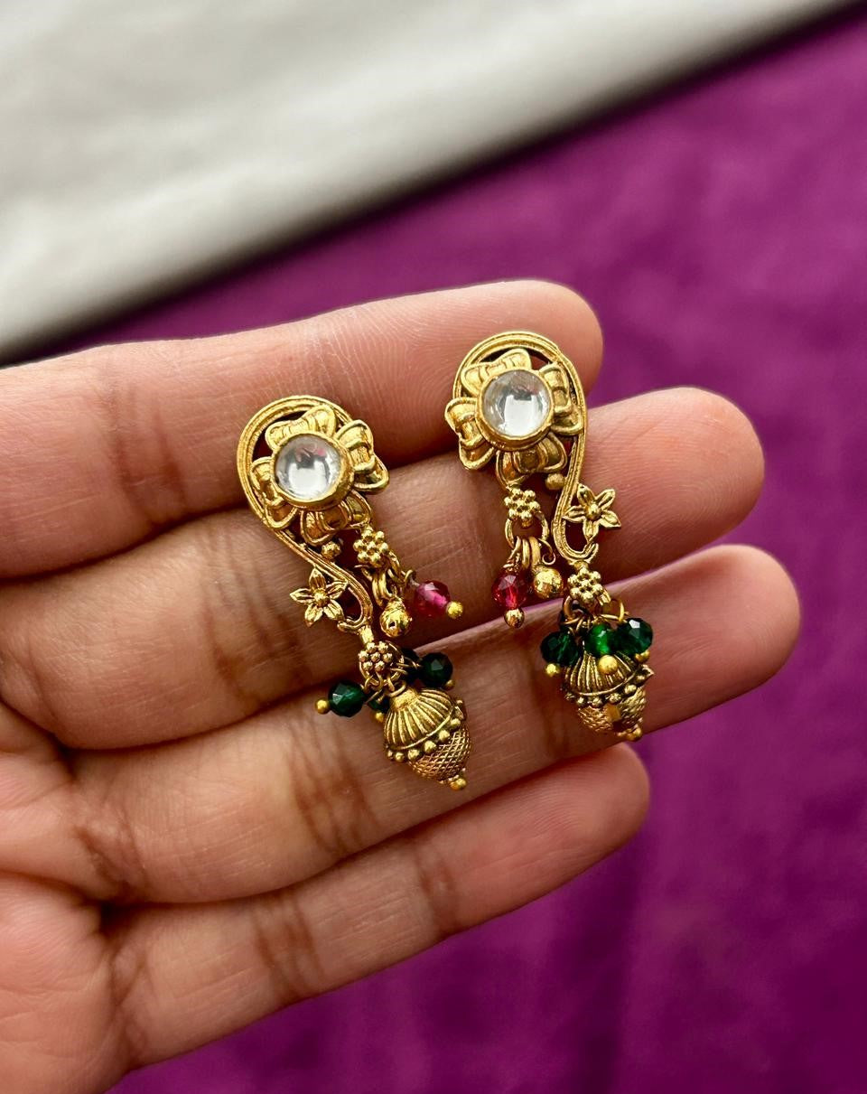 Gold earrings with gemstones held in a hand against a purple background
