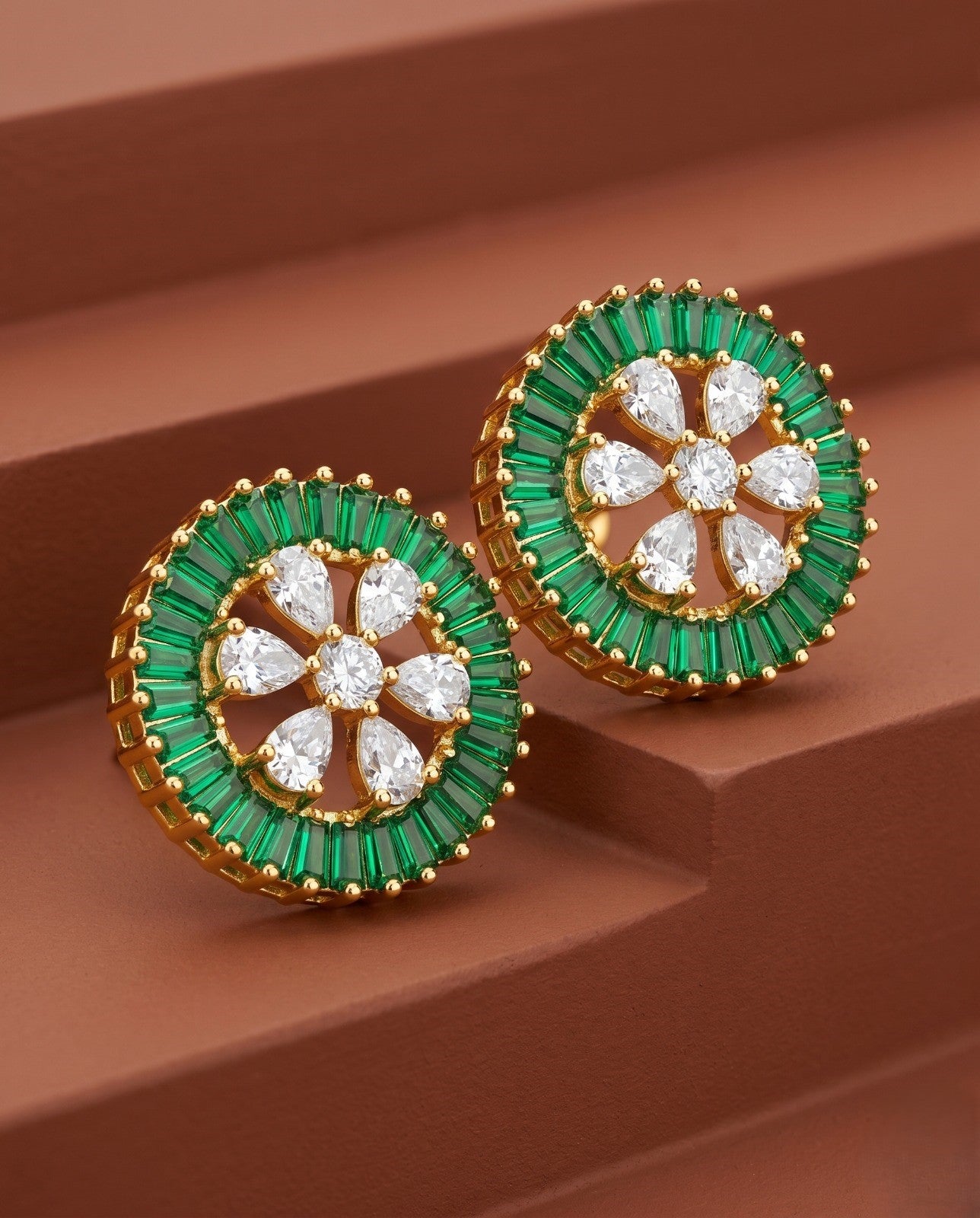 Gold earrings with green and clear gemstones on a brown surface