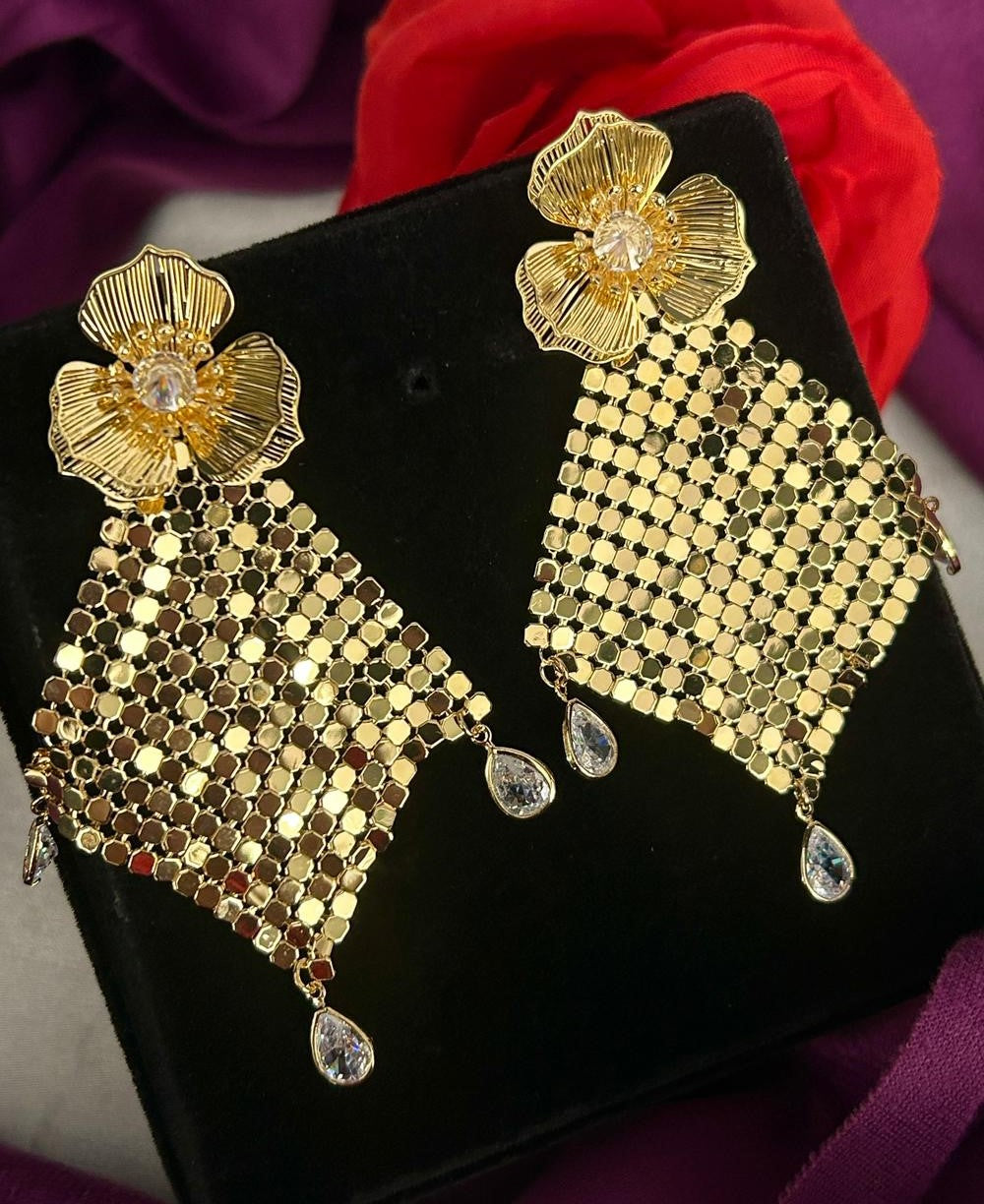 Gold earrings with intricate designs on a black stand against a purple fabric background