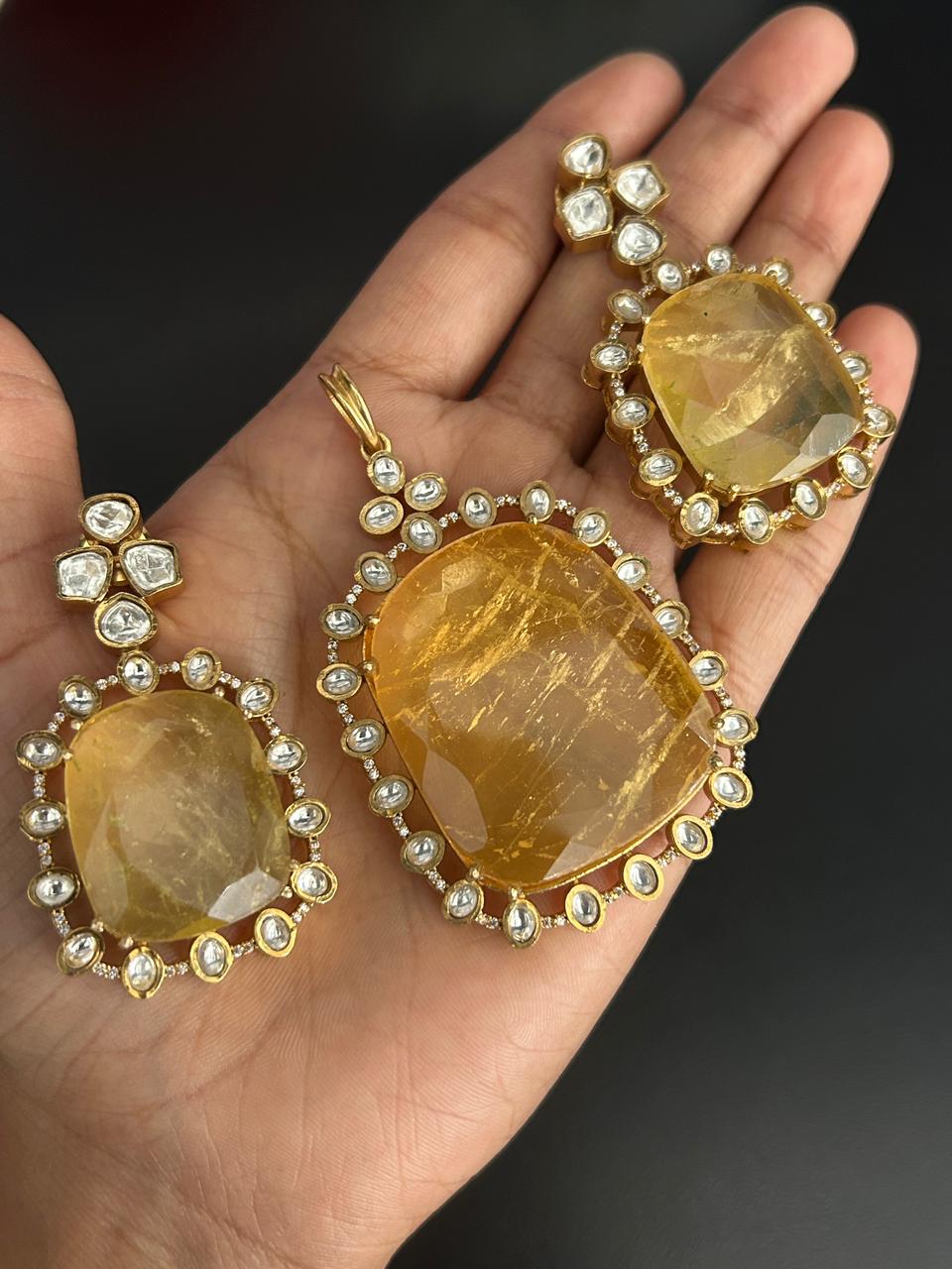 Gold earrings with large yellow gemstones held in a hand against a dark background