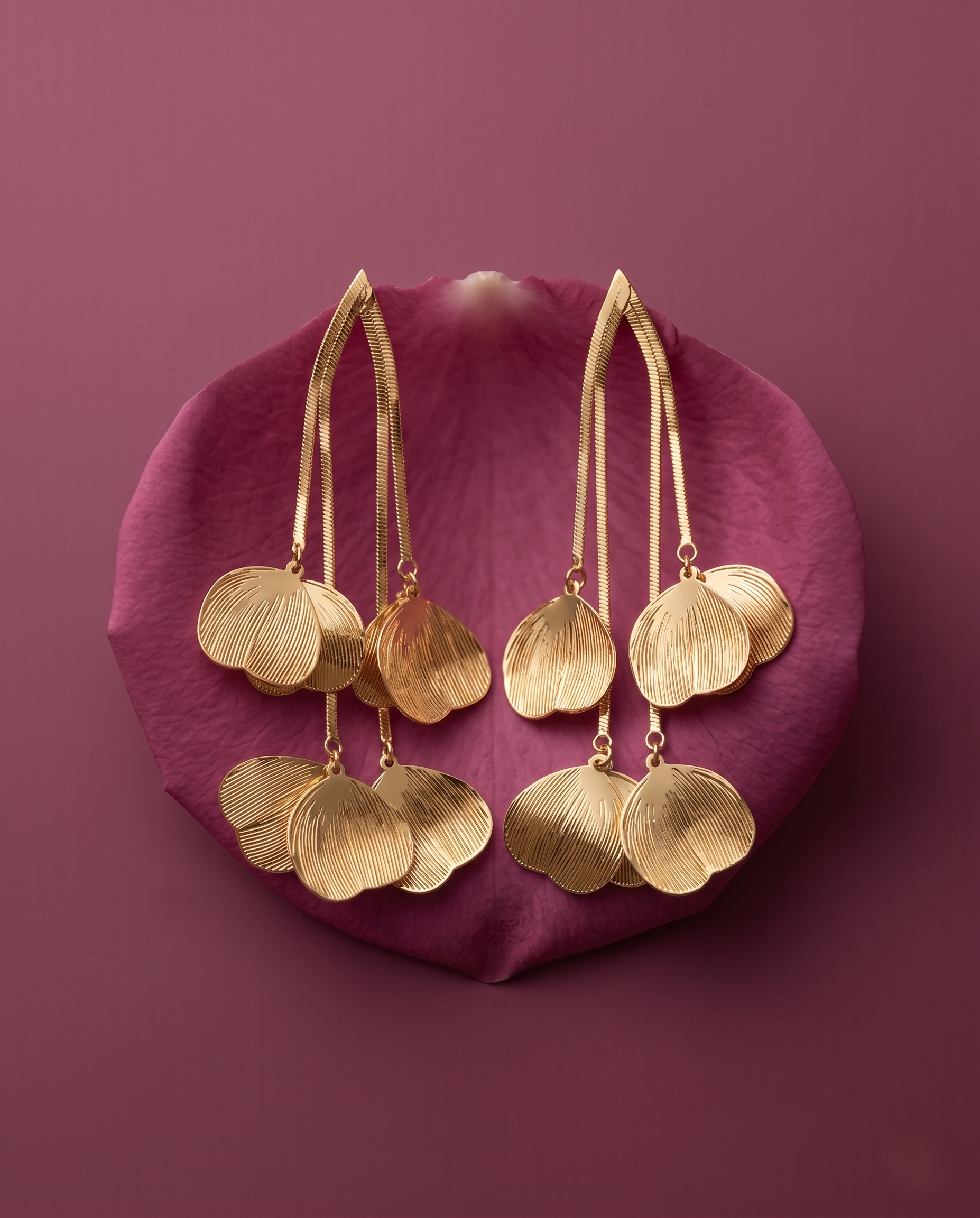 Gold earrings with leaf-like designs on a pink petal against a purple background