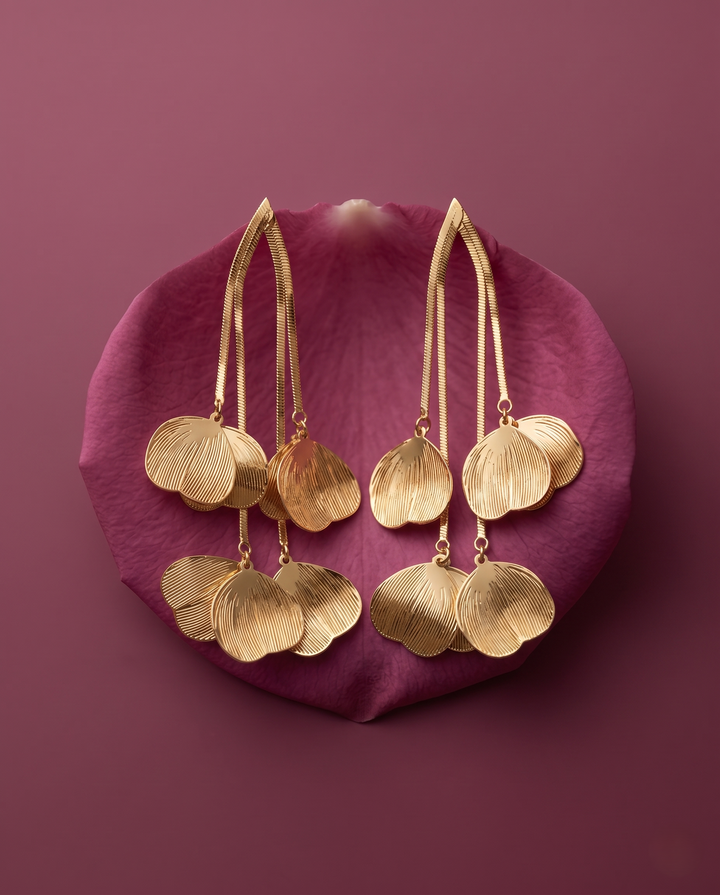 Gold earrings with leaf-like designs on a pink petal against a purple background