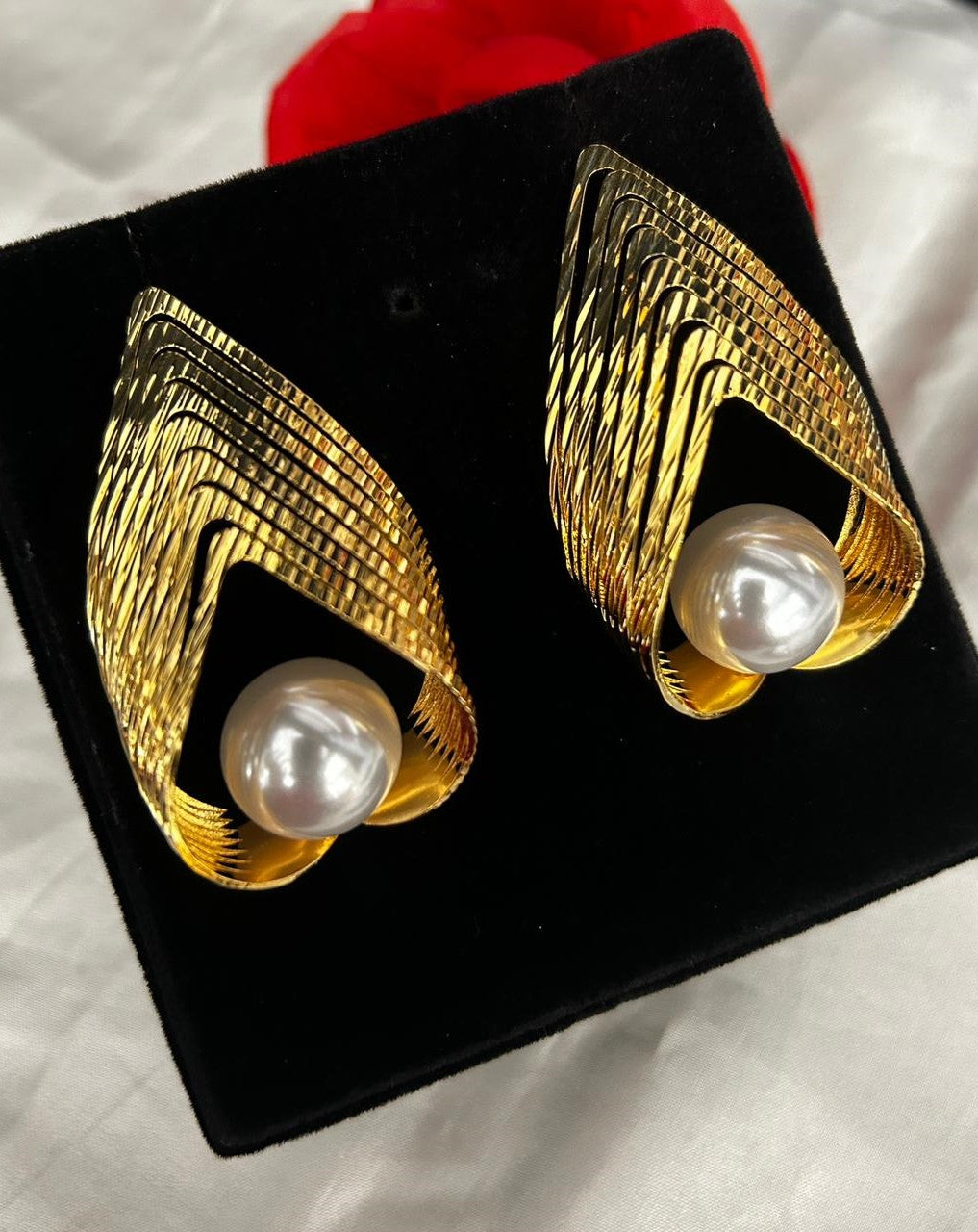 Gold earrings with pearl centers on a black stand against a white background