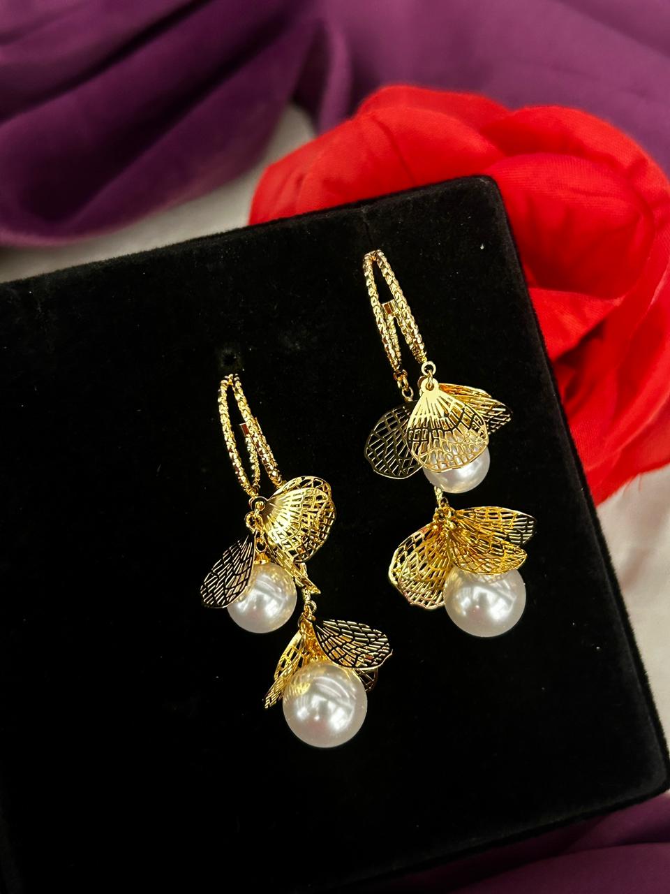 Gold earrings with pearl drops on a black display box against a purple fabric background