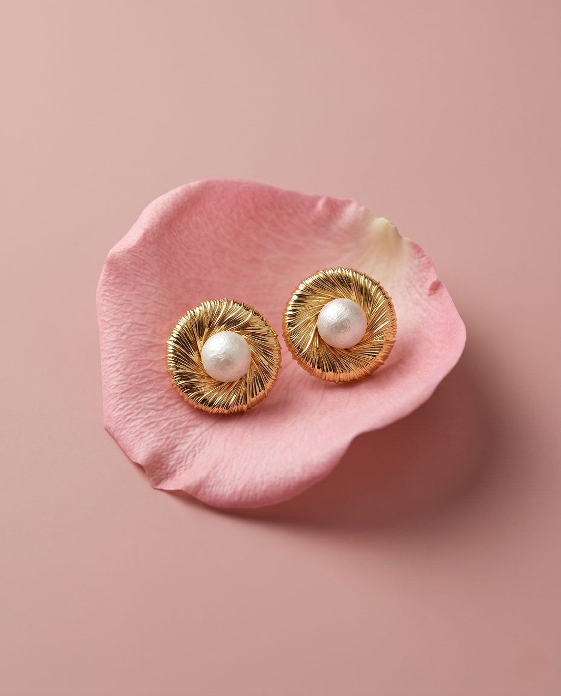 Gold earrings with pearls on a pink petal against a pink background
