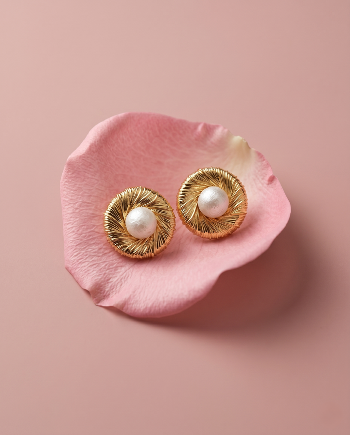 Gold earrings with pearls on a pink petal against a pink background