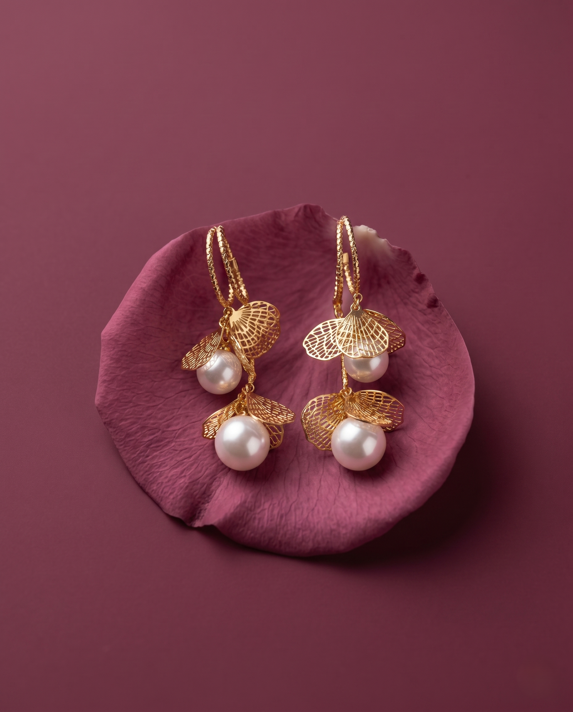 Gold earrings with pearls on a pink petal against a purple background