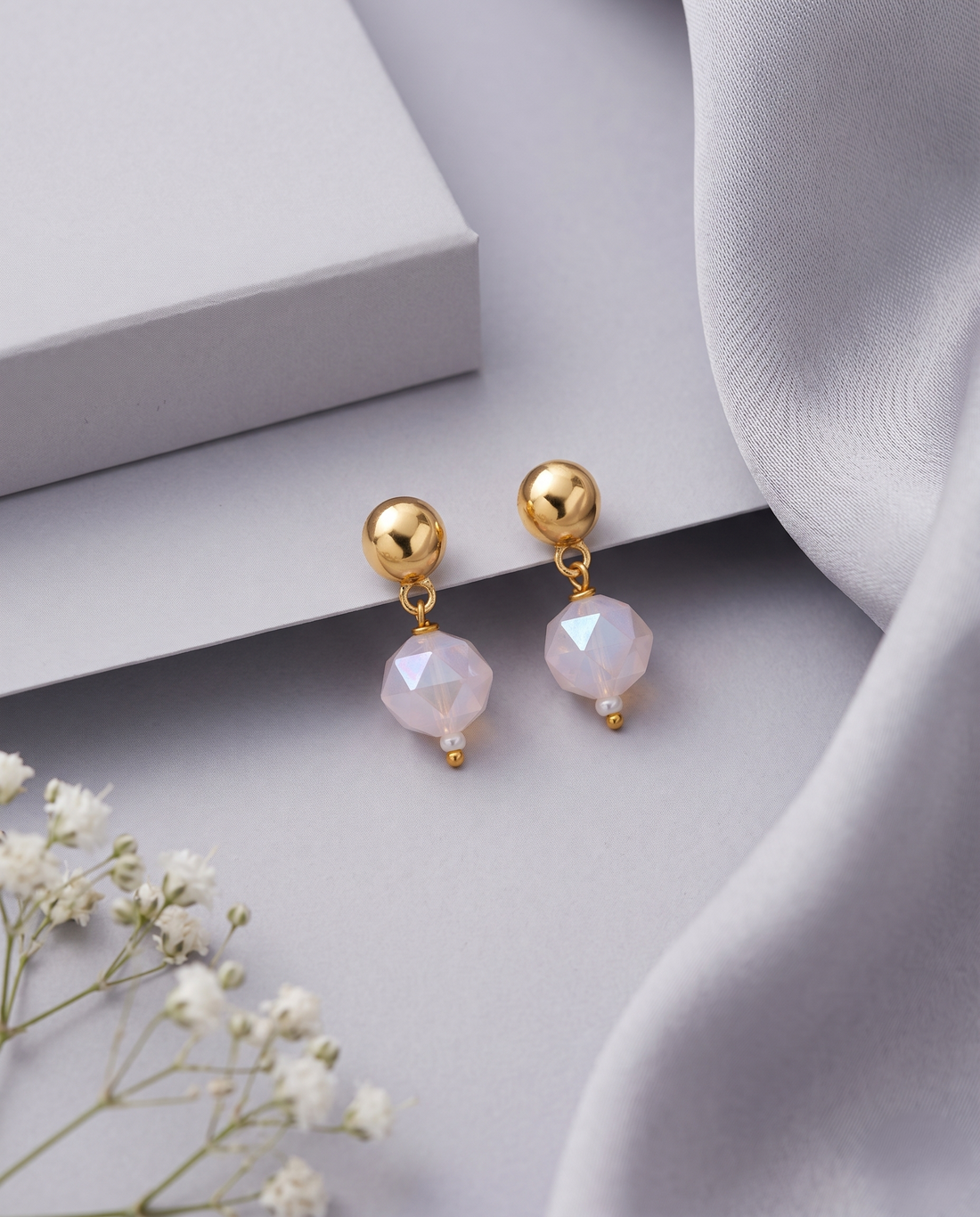Gold earrings with pink beads on light gray surface with white flowers.
