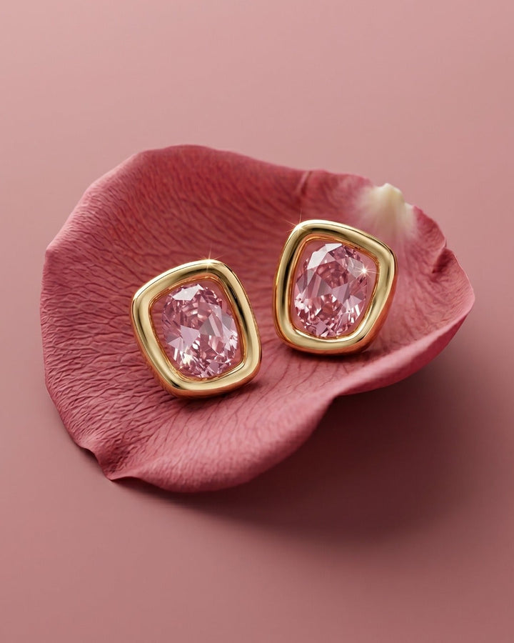 Gold earrings with pink gemstones on a pink petal
