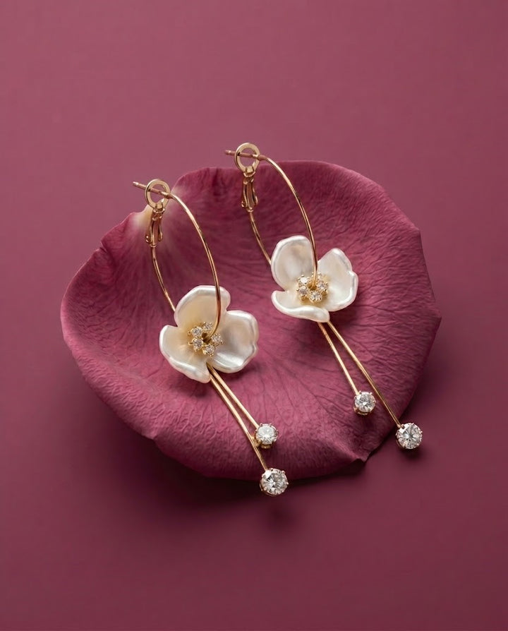 Gold hoop earrings with white floral designs on a pink petal against a purple background