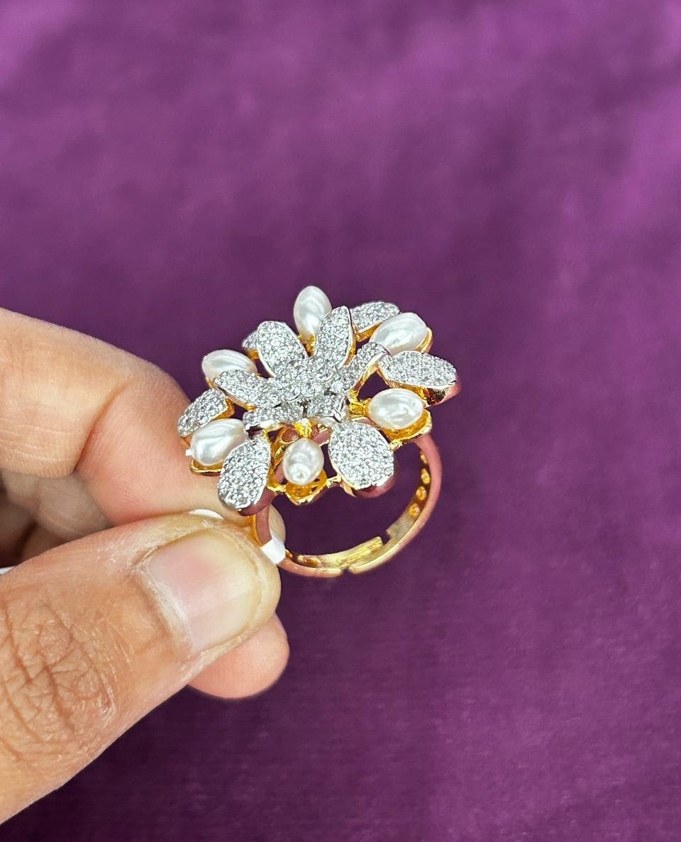 Gold ring with floral design held by a hand against a purple background