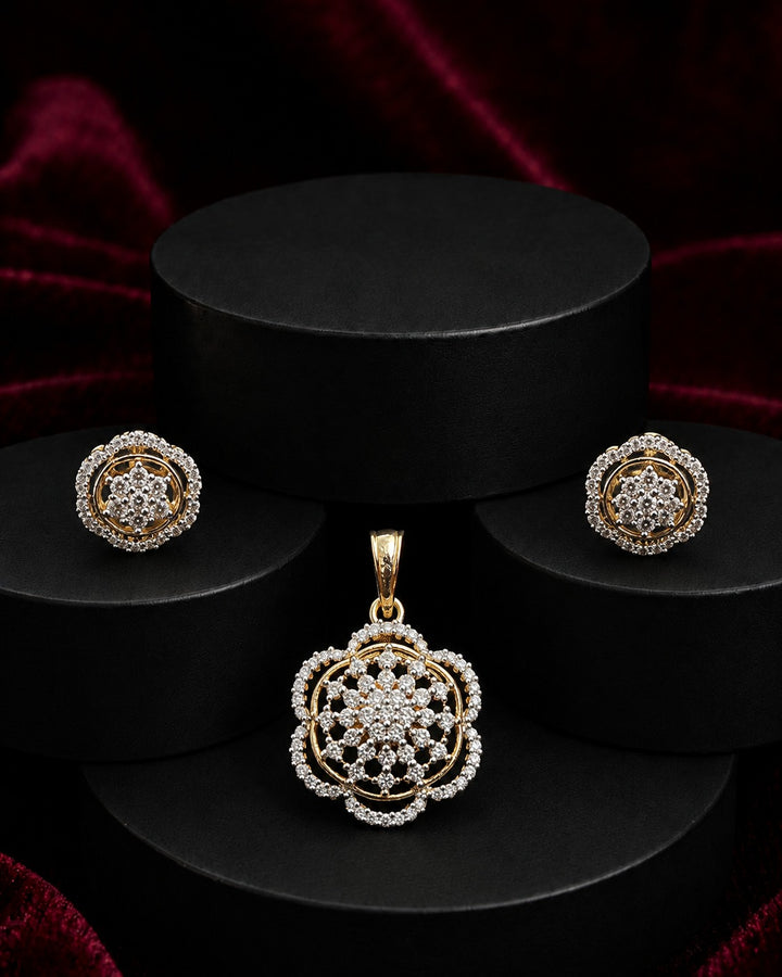 Gold jewelry set featuring a floral pendant, matching stud earrings, and a chain link necklace, displayed on black cylindrical pedestals against a dark red velvet background.