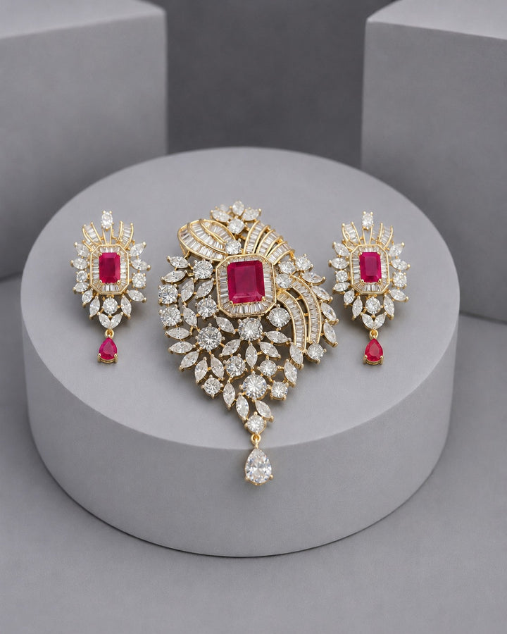 Gold jewelry set featuring a large central brooch and two matching drop earrings, decorated with clear crystals and square pink gemstones, displayed on a round gray pedestal.