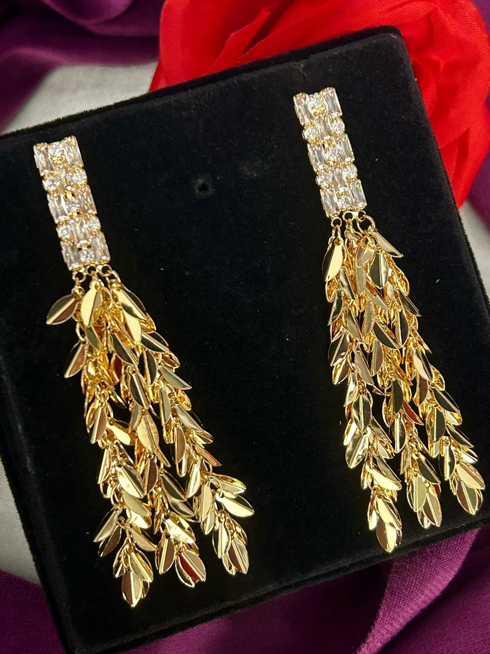 Gold leaf earrings on a black velvet stand with red fabric in the background