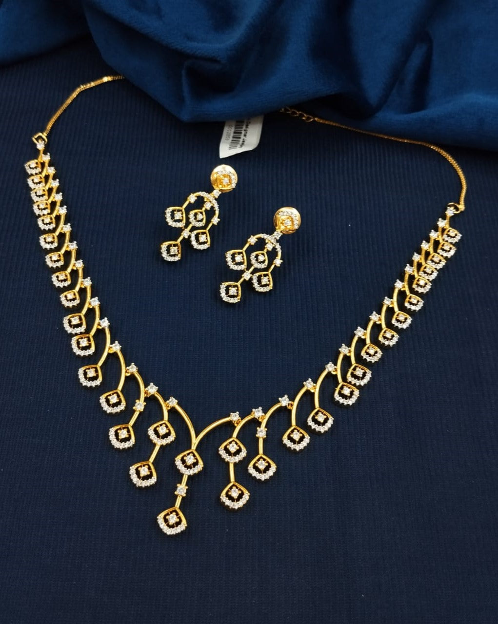 Gold necklace and earrings on a dark blue fabric background