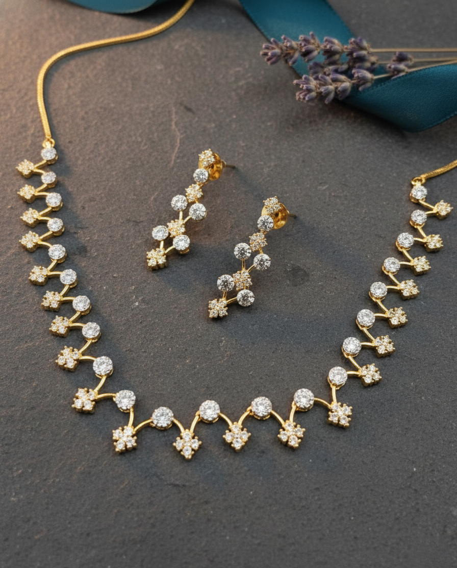 Gold necklace and earrings on a dark surface with lavender flowers.
