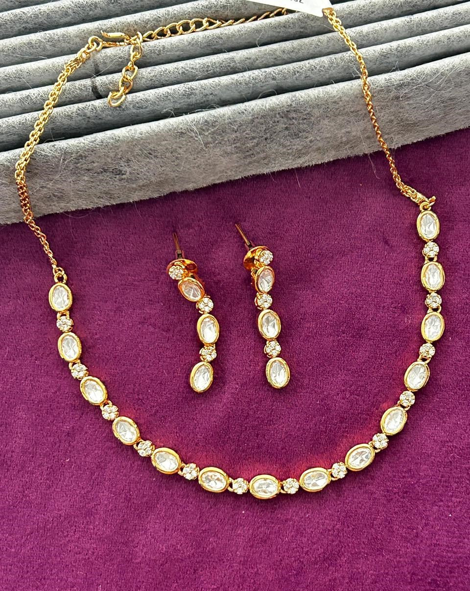 Gold necklace and earrings on a purple surface with gray wooden planks in the background
