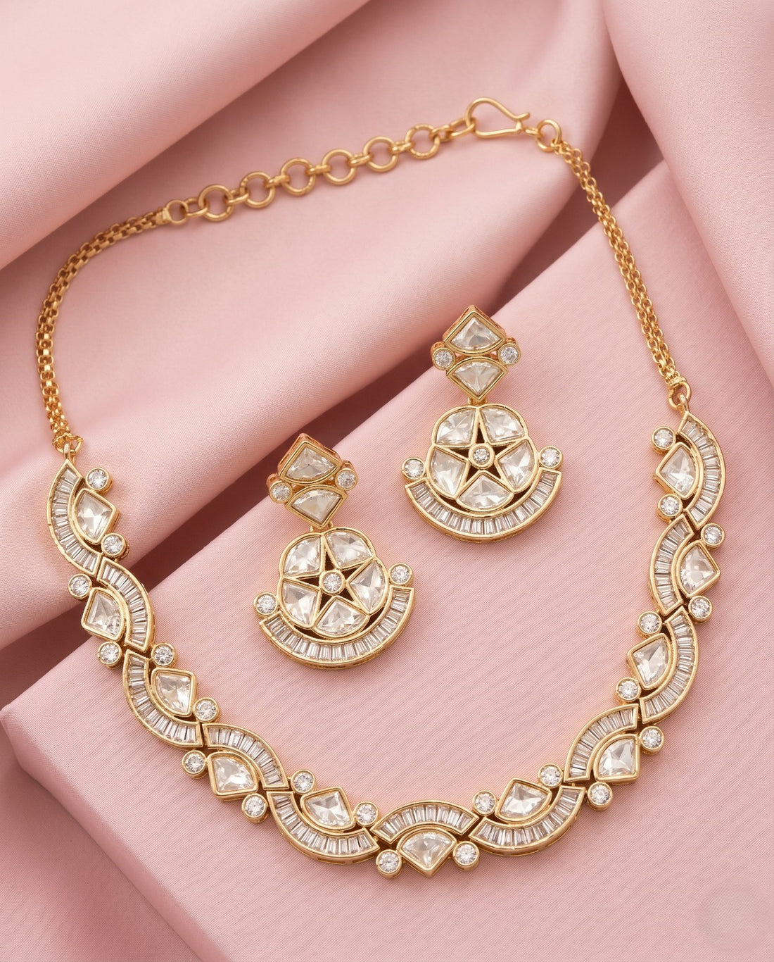 Gold necklace and earrings set on a pink fabric background