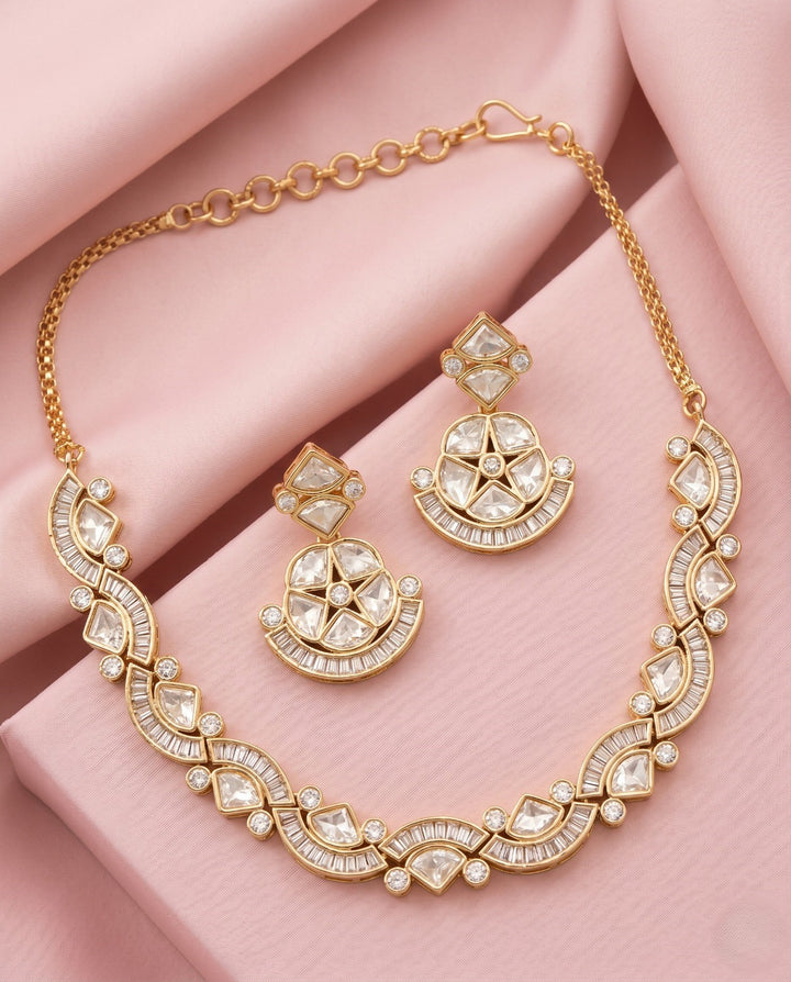 Gold necklace and earrings set on a pink fabric background