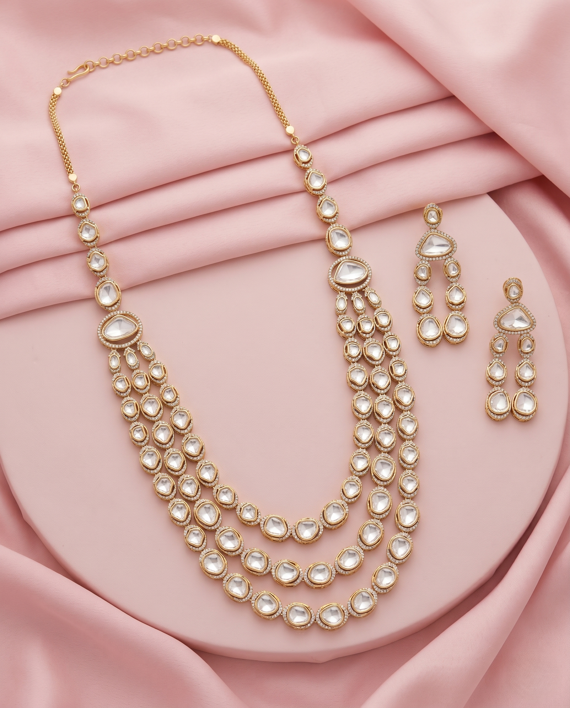 Gold necklace and earrings set on a pink fabric background