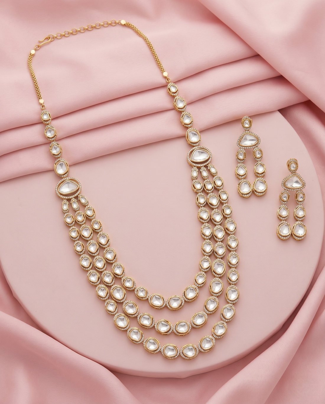 Gold necklace and earrings set on a pink fabric background