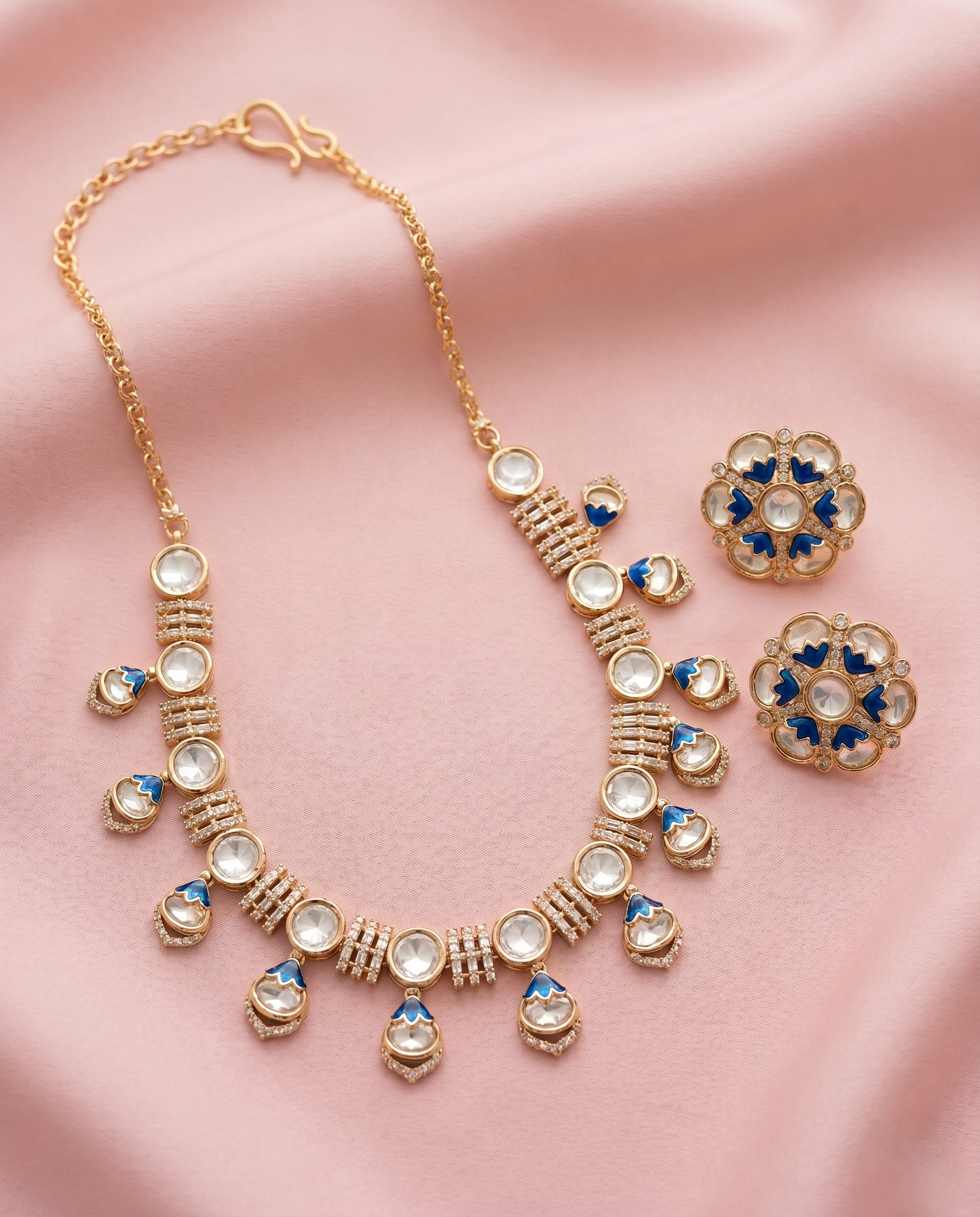 Gold necklace and earrings with blue and white stones on a pink fabric background