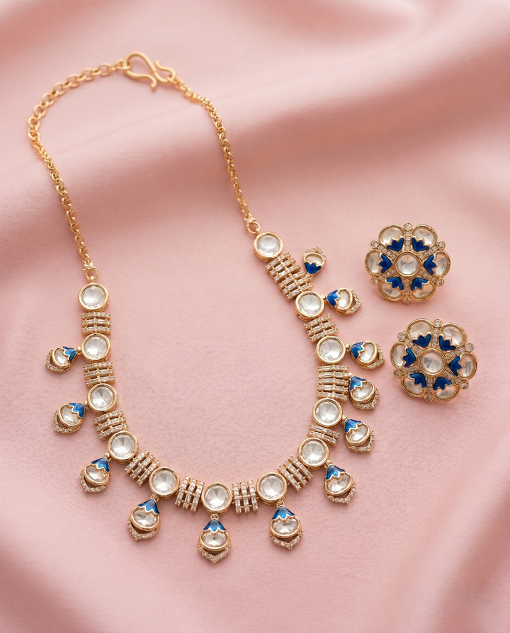 Gold necklace and earrings with blue and white stones on a pink fabric background