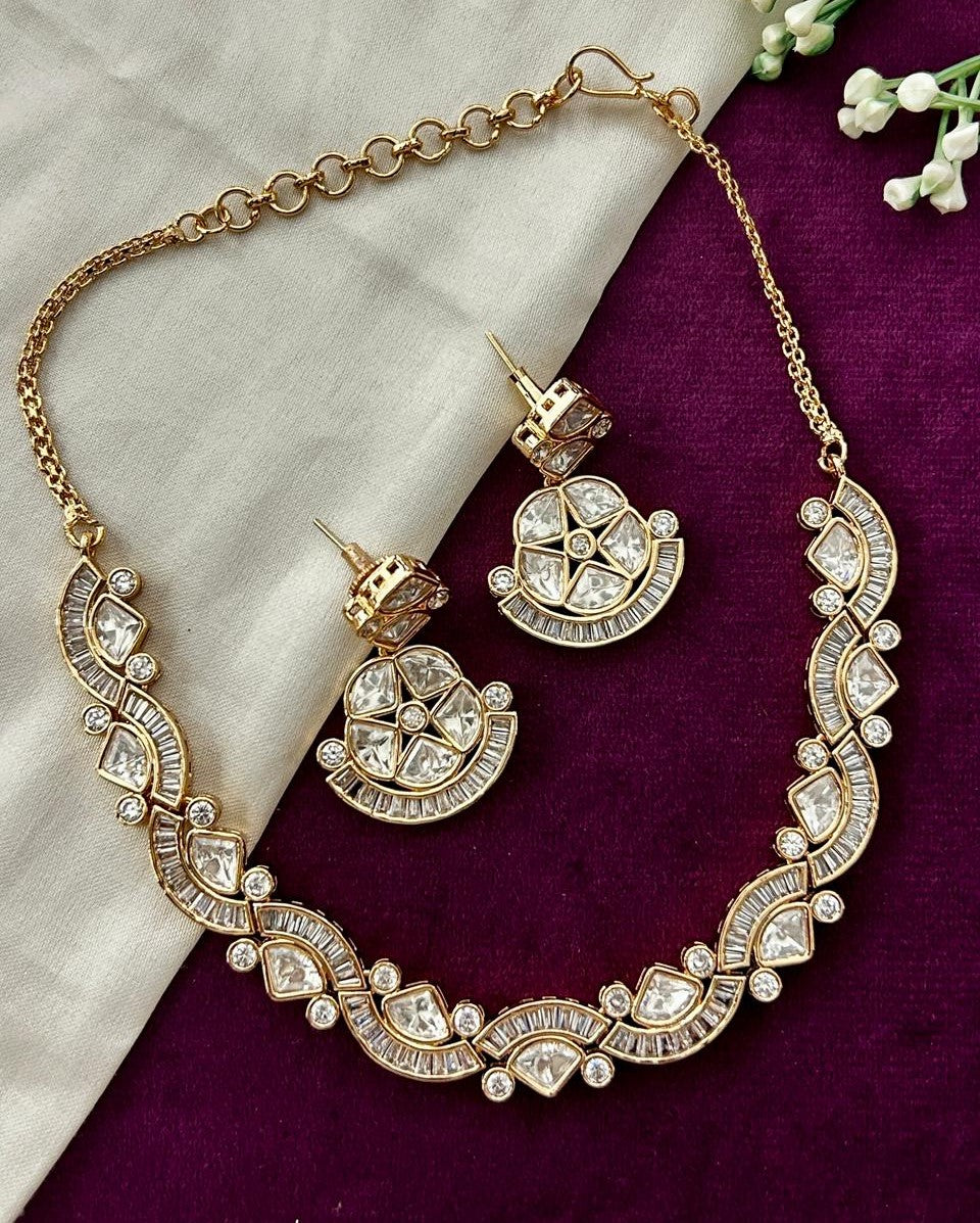 Gold necklace and earrings with crystal embellishments on a purple and white fabric background