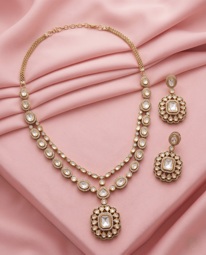 Gold necklace and earrings set on a pink fabric background