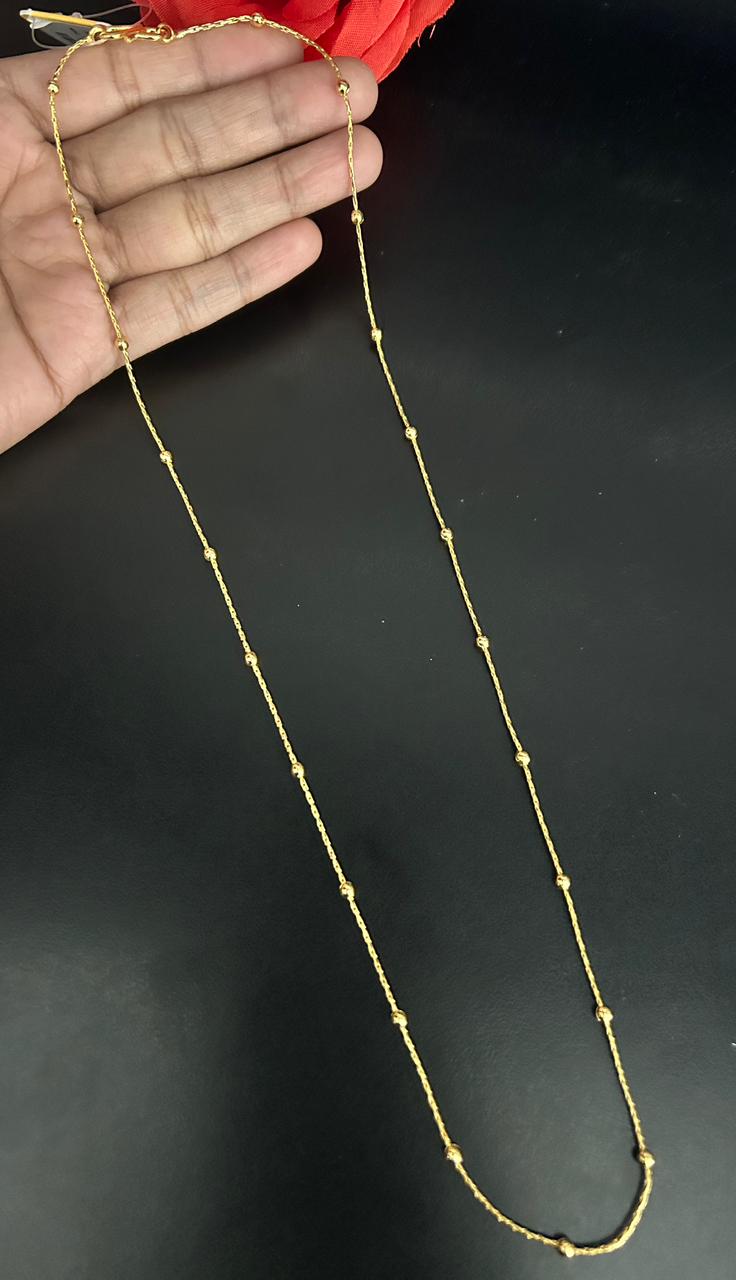 Gold necklace by a hand against a dark background