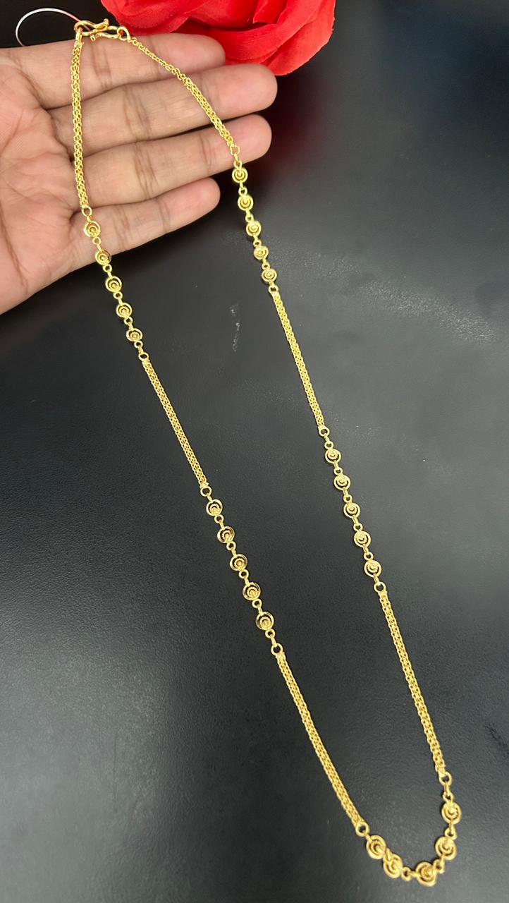 Gold necklace held by a hand against a dark background