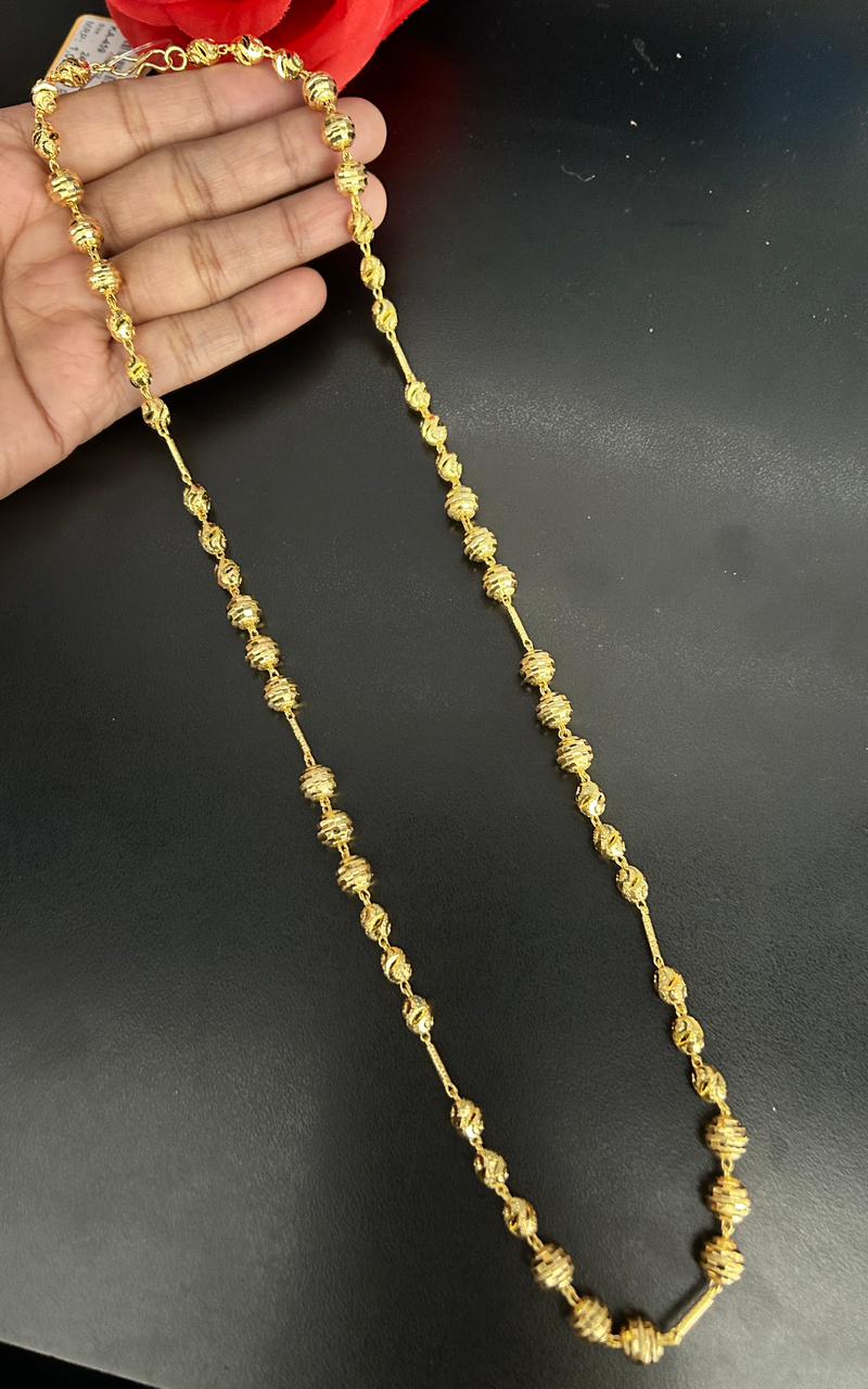 Gold necklace held by a hand on a black background