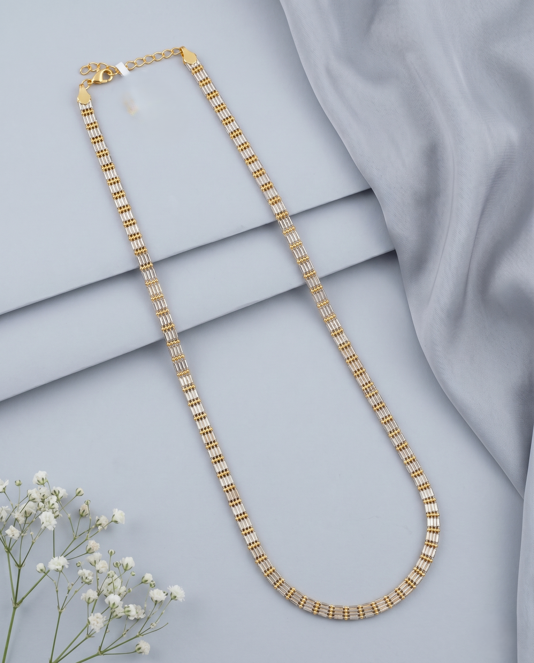 Gold necklace on a light gray fabric background with small white flowers.