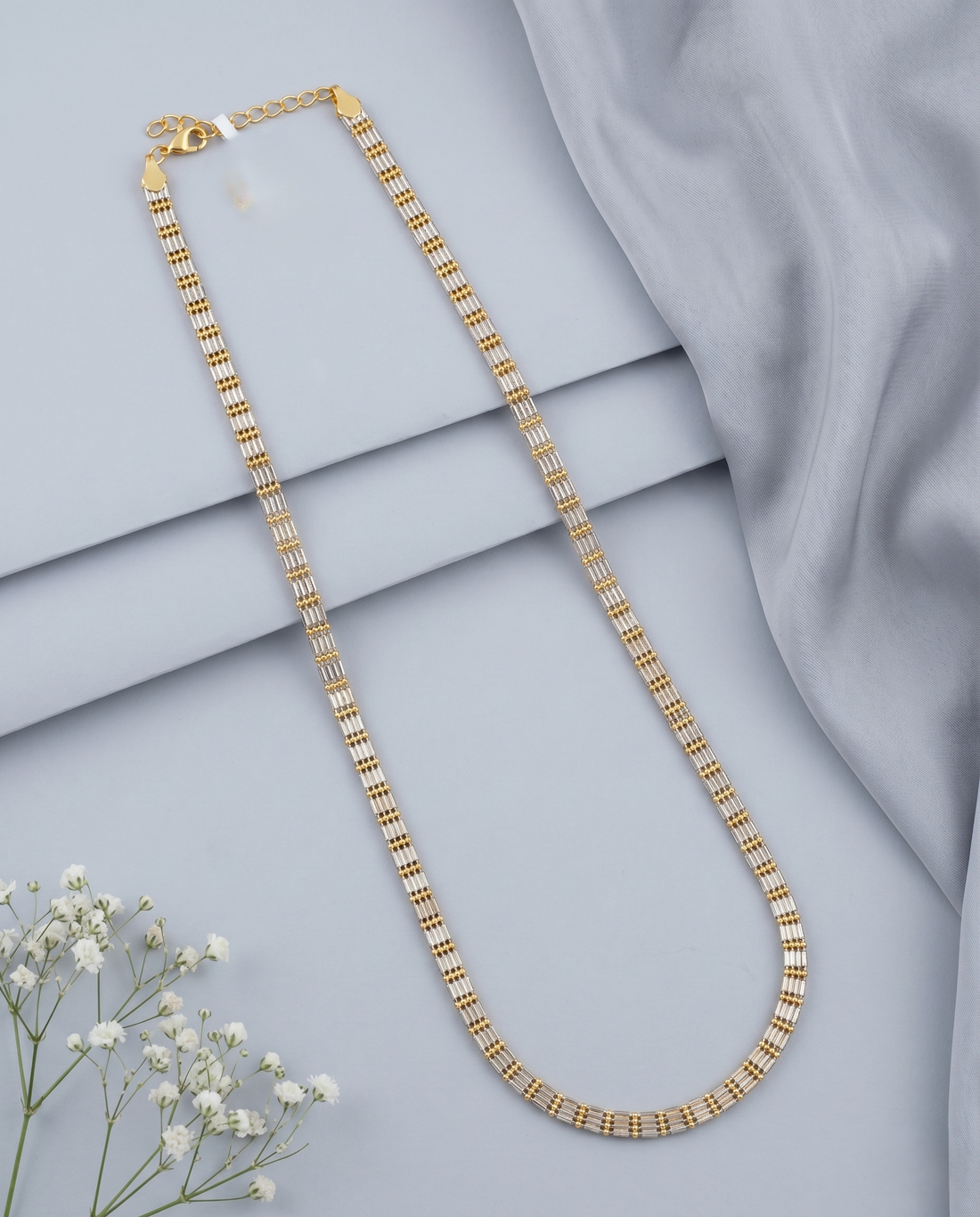 Gold necklace on a light gray fabric background with small white flowers.