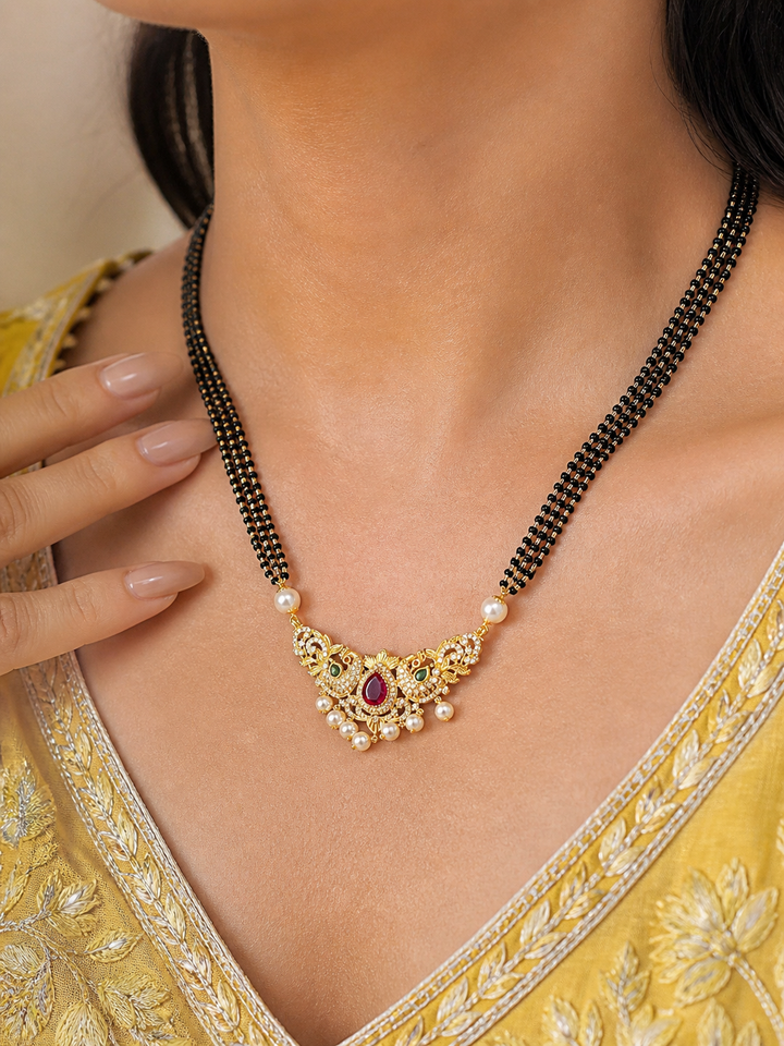 Gold necklace with a red gemstone on a person wearing a yellow saree.