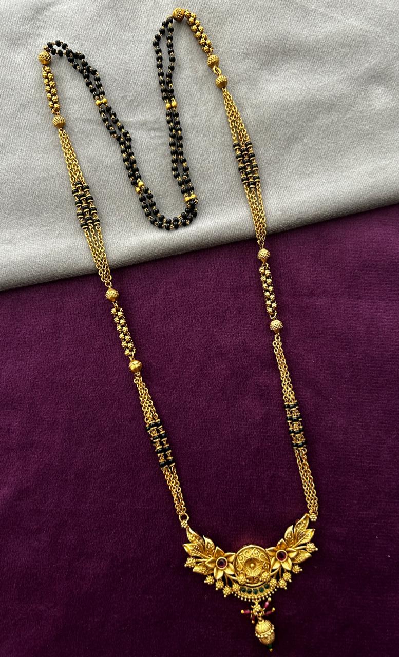 Gold necklace with black beads on a purple and gray fabric background