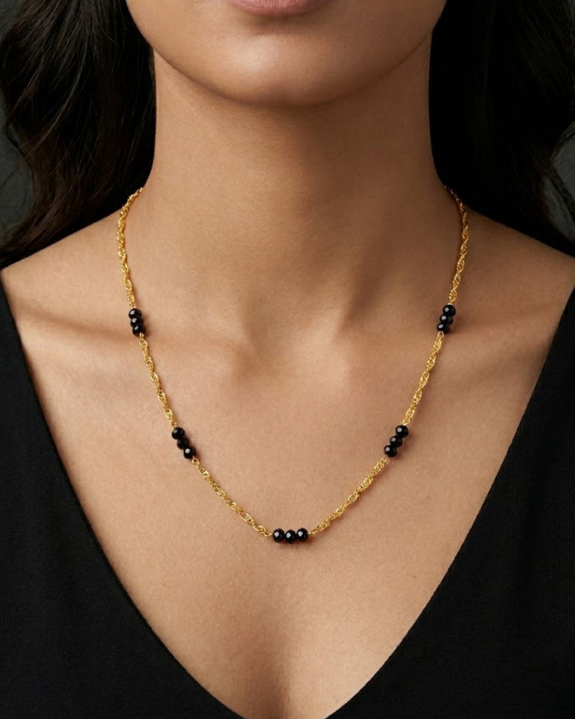Gold necklace with black beads worn by a model against a dark background