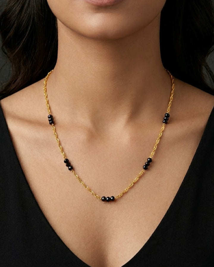 Gold necklace with black beads worn by a model against a dark background
