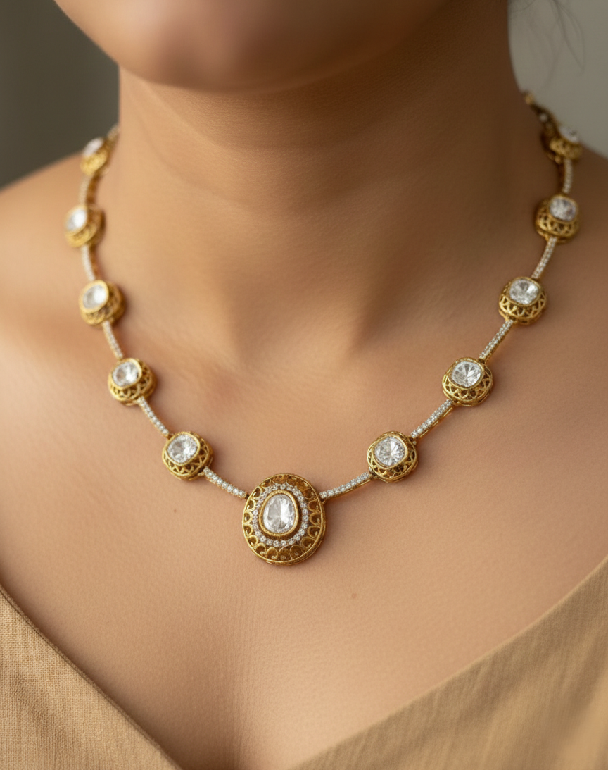 Gold necklace with circular designs and clear stones on a person wearing a beige top.