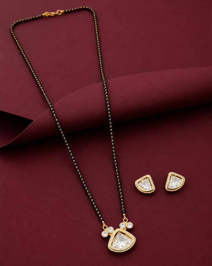 Gold necklace with pendant and matching earrings on a maroon fabric background