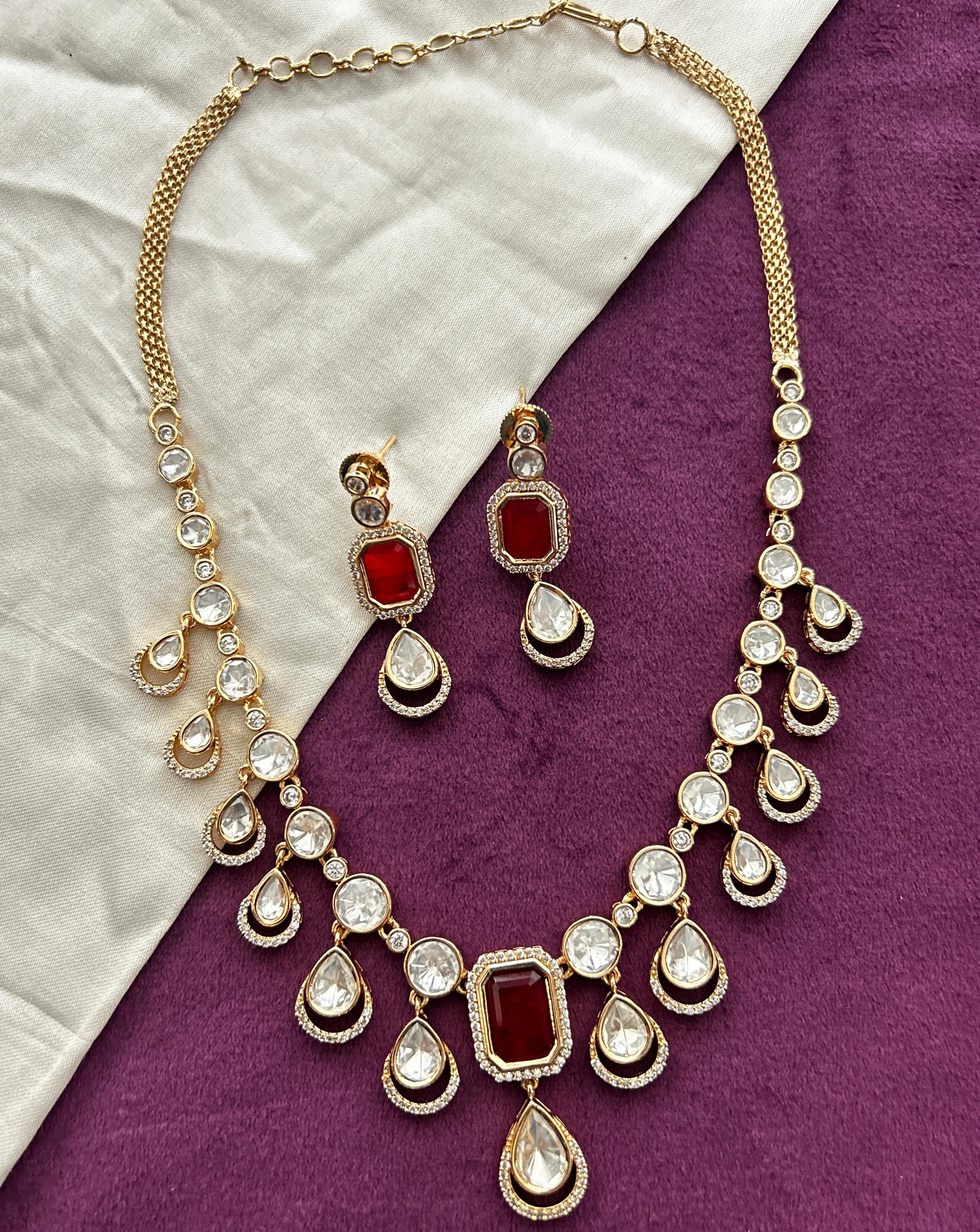 Gold necklace with red and clear stones on a purple and white fabric background