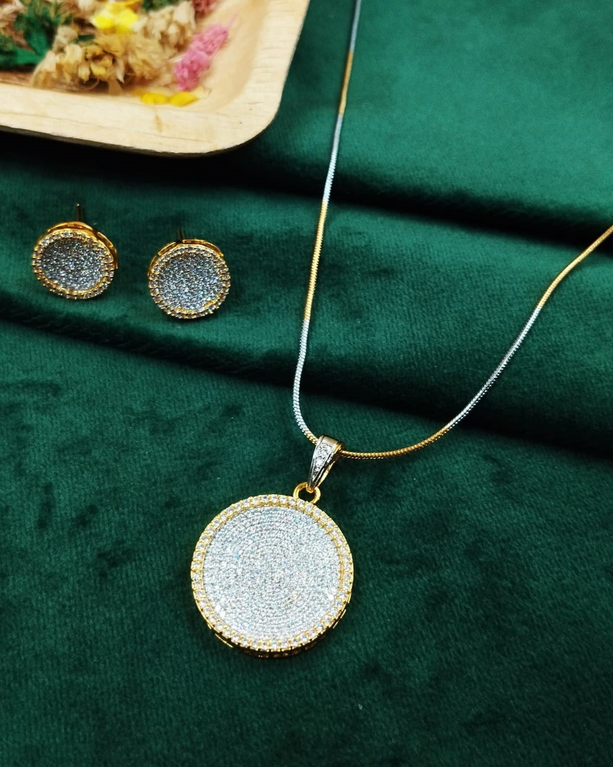 Gold necklace with round pendant and matching earrings on a green fabric background